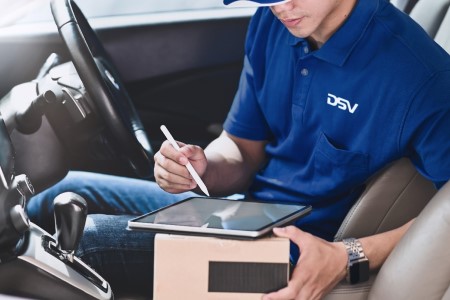 a DSV courier driver in a car with a parcel and a tablet in his hand